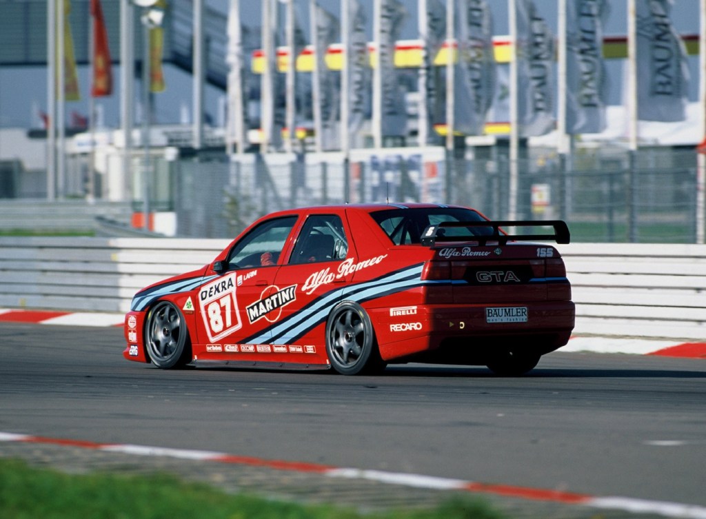 A red 1993 Alfa Romeo 155 2.5 TI DTM race car drives around the track