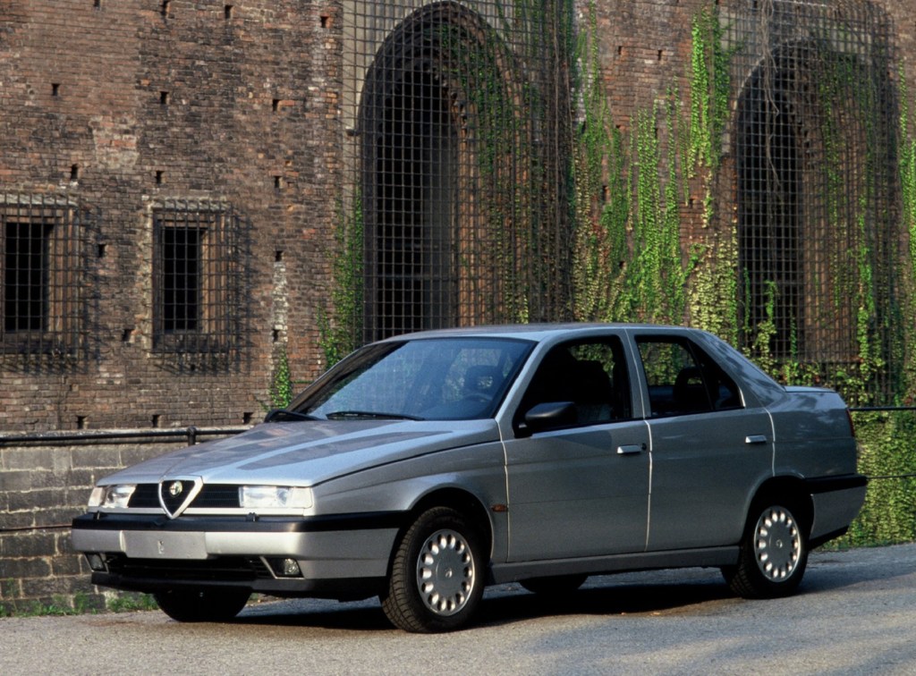 A silver 1993 Alfa Romeo 155 in front of an ivy-covered stone building