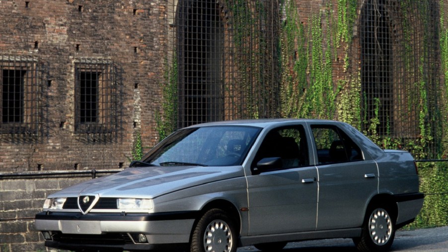 A silver 1993 Alfa Romeo 155 in front of an ivy-covered stone building