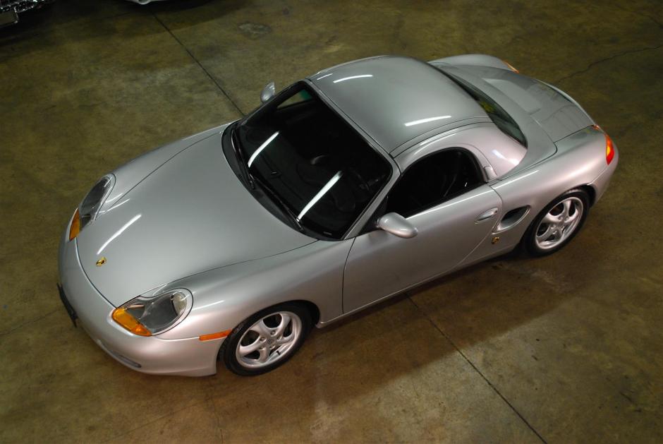 A silver 1997 Porsche Boxster with a hard top sits in the middle of a garage.