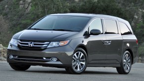 A grey 2015 Honda Odyssey parked near a green mountain.