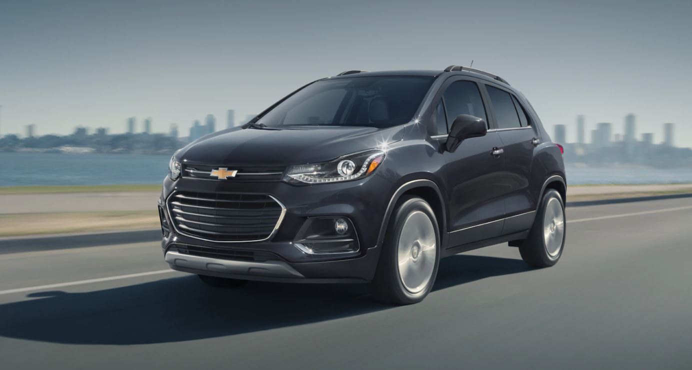A black Chevrolet Trax SUV drives by a cityscape.