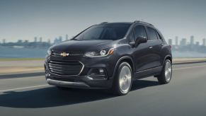 A black Chevrolet Trax SUV drives by a cityscape.
