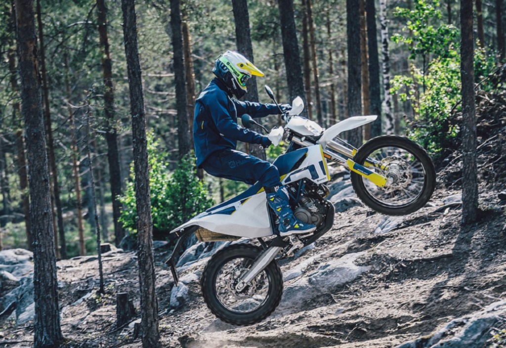 A rider jumps a white 2020 Husqvarna 701 Enduro through a forest