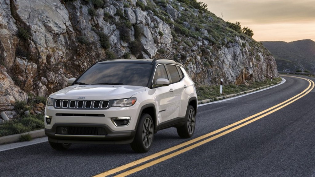 A white 2020 Jeep Compass drives next to a rocky hill