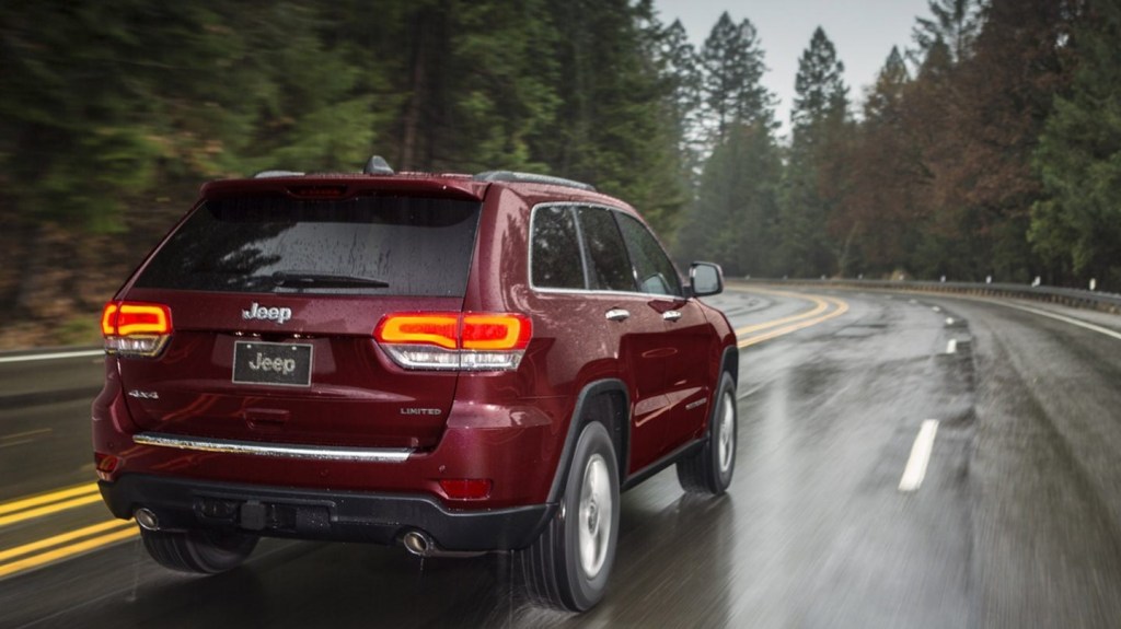 The rear view of a red 2020 Jeep Grand Cherokee Limited driving through a rainy forest