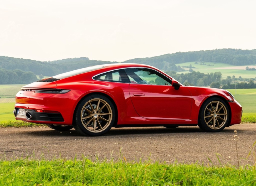 The rear 3/4 view of a red 2020 Porsche 911 Carrera among rolling green hills