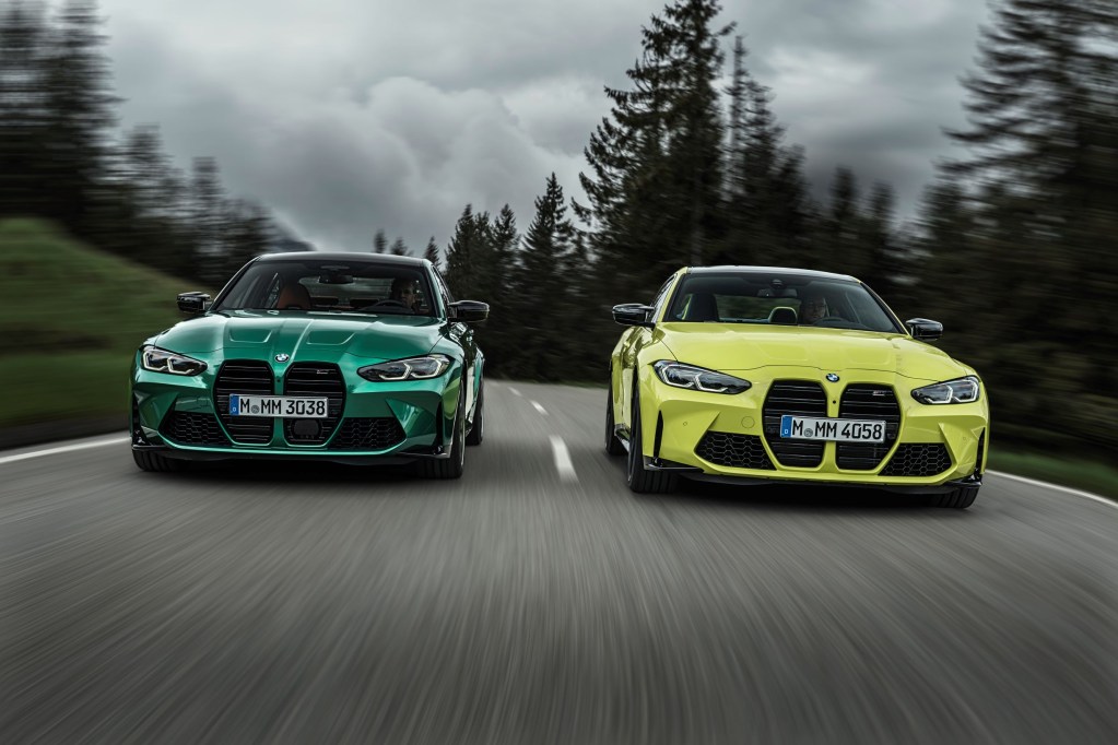 A green 2021 BMW M3 Competition and yellow BMW M4 Competition drive down a forested mountain road