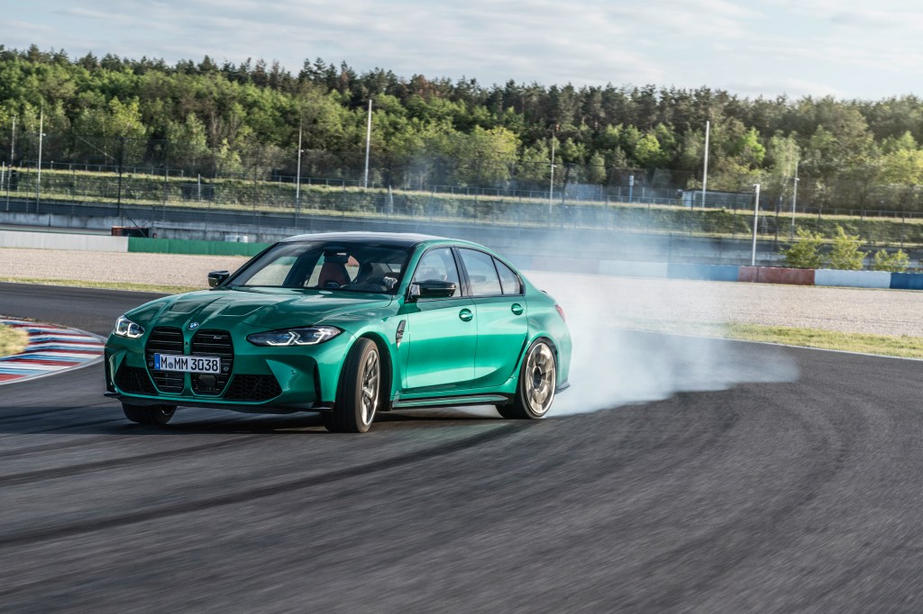 The front 3/4 view of a green 2021 M3 sliding around a racetrack