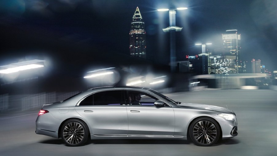 A silver 2021 Mercedes S-Class drives through a bright-lit night city