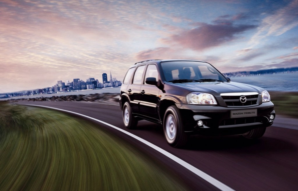 a black 2005 Mazda Tribute SUV driving at speed on a scenic road with an urban view