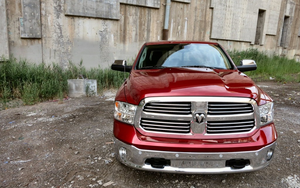 A red Ram 1500 pickup parked in front of a brown shed.