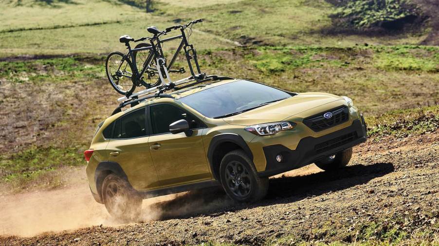 a gold 2021 subaru Crosstrek subcompact crossover SUV off-roading with a loaded bike rack up top.