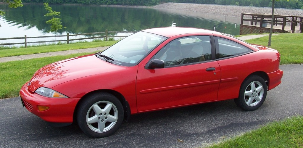 red Chevy Cavalier parked in fron t of a serene pond