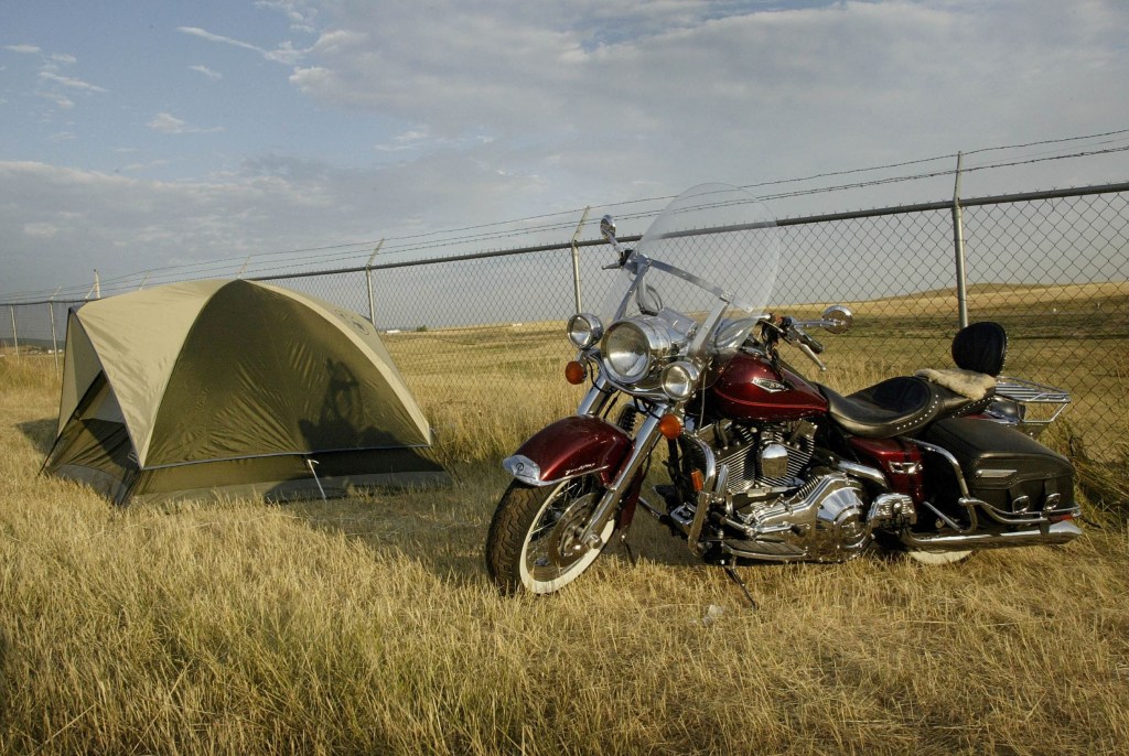 A red cruiser motorcycle parked next to a green camping tent in a grassy field