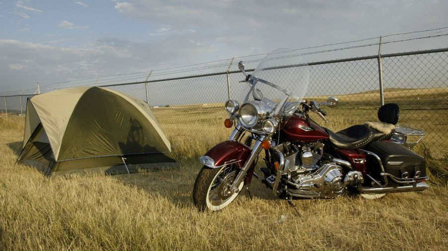 A red cruiser motorcycle parked next to a green camping tent in a grassy field