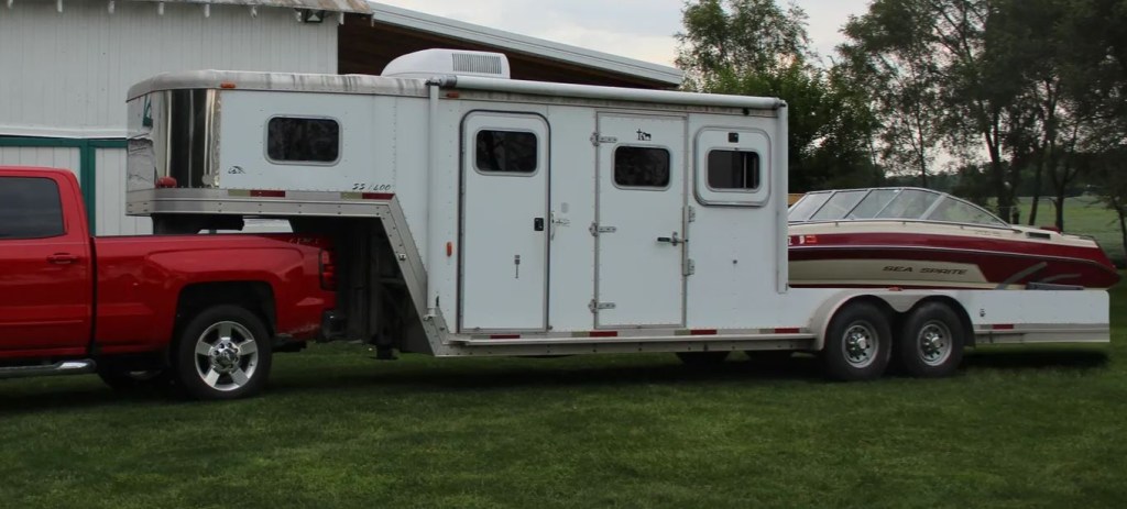 A white horse trailer has been converted to carry a boat in the rear.