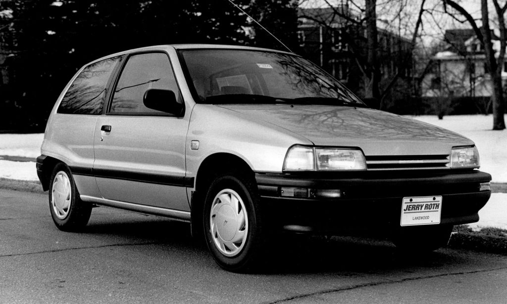 A black and white photo of a small Daihatsu Charade hatchback parked by a curb.