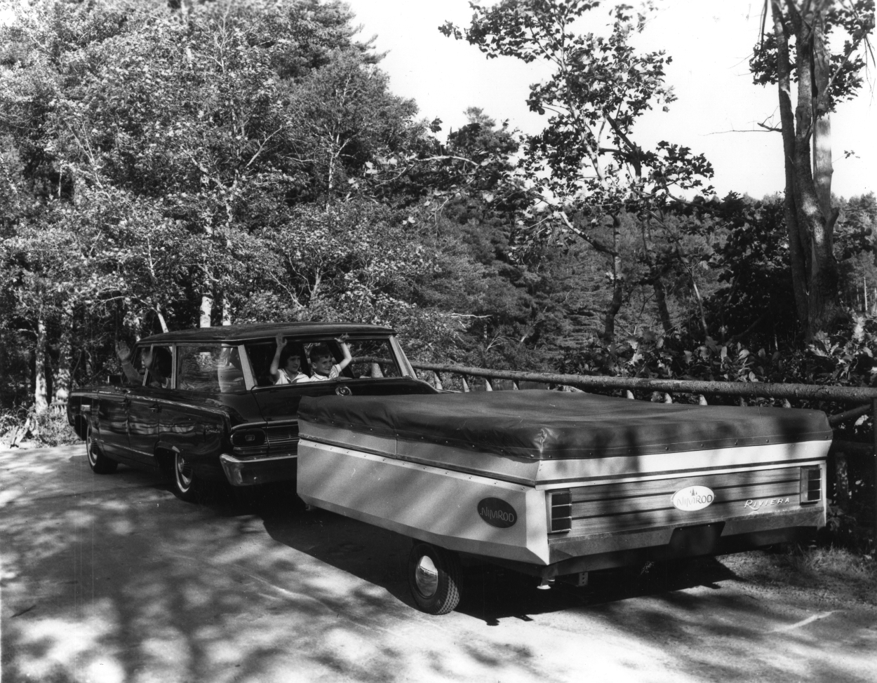 An old black and white photo of a family towing a pop-up camper