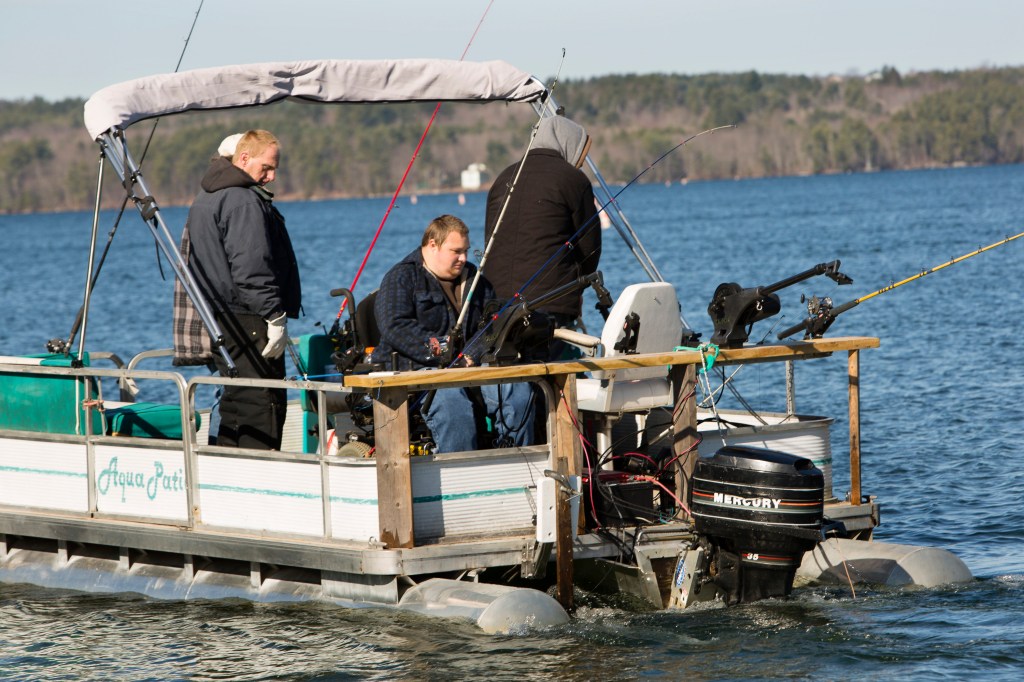 Men fishing off of a pontoon boat in a lake