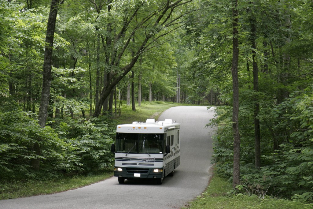 An RV driving down a road in the woods