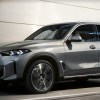 A gray BMW X5 midsize SUV is driving on the road.