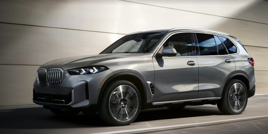 A gray BMW X5 midsize SUV is driving on the road.