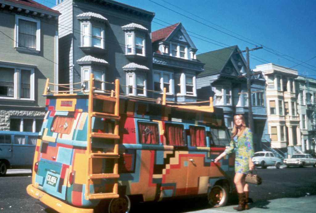 A hippie girl stands next to a Volkswagen bus painted in a bold design, San Francisco, California, July, 1967.