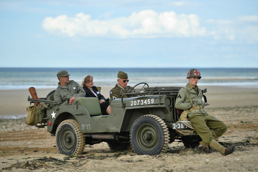 People wearing vintage-style military costumes sit in a US military Willy’s Jeep at a D-Day 75th Anniversary event