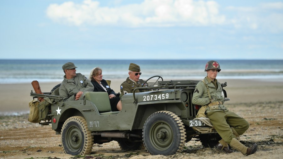 People wearing vintage-style military costumes sit in a US military Willy’s Jeep at a D-Day 75th Anniversary event