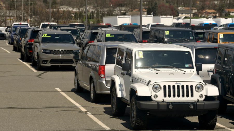 car dealership lot with a white jeep and other cars with model years and prices highlighted