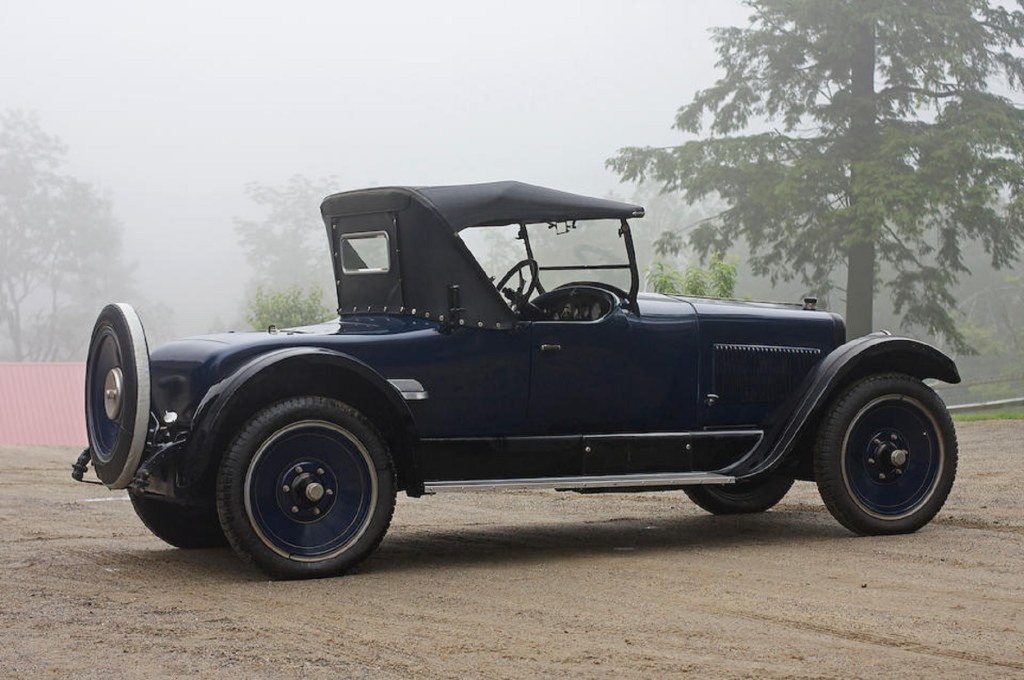 The rear 3/4 view of a blue 1924 Wills Sainte Claire Model A-68 Roadster in a foggy forest