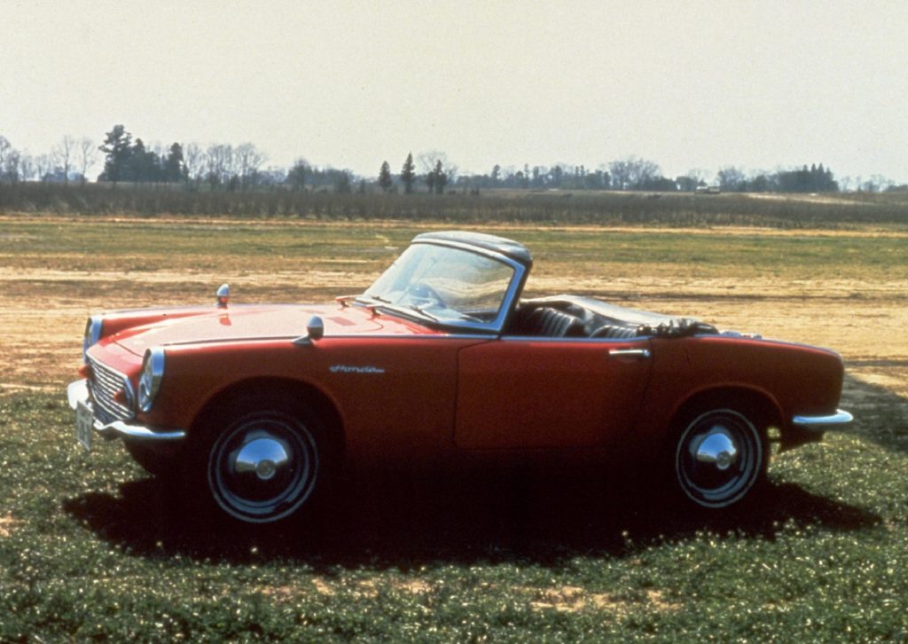 An orange 1964 Honda S600 roadster on a grassy field