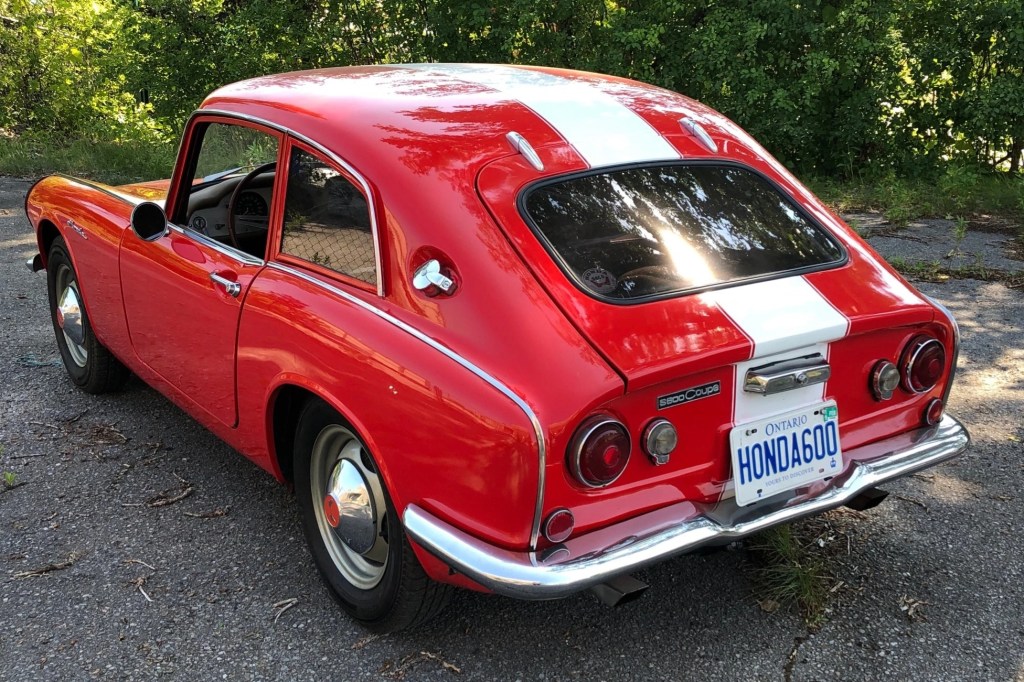 The rear 3/4 view of a red-with-white-stripes 1966 Honda S600 coupe