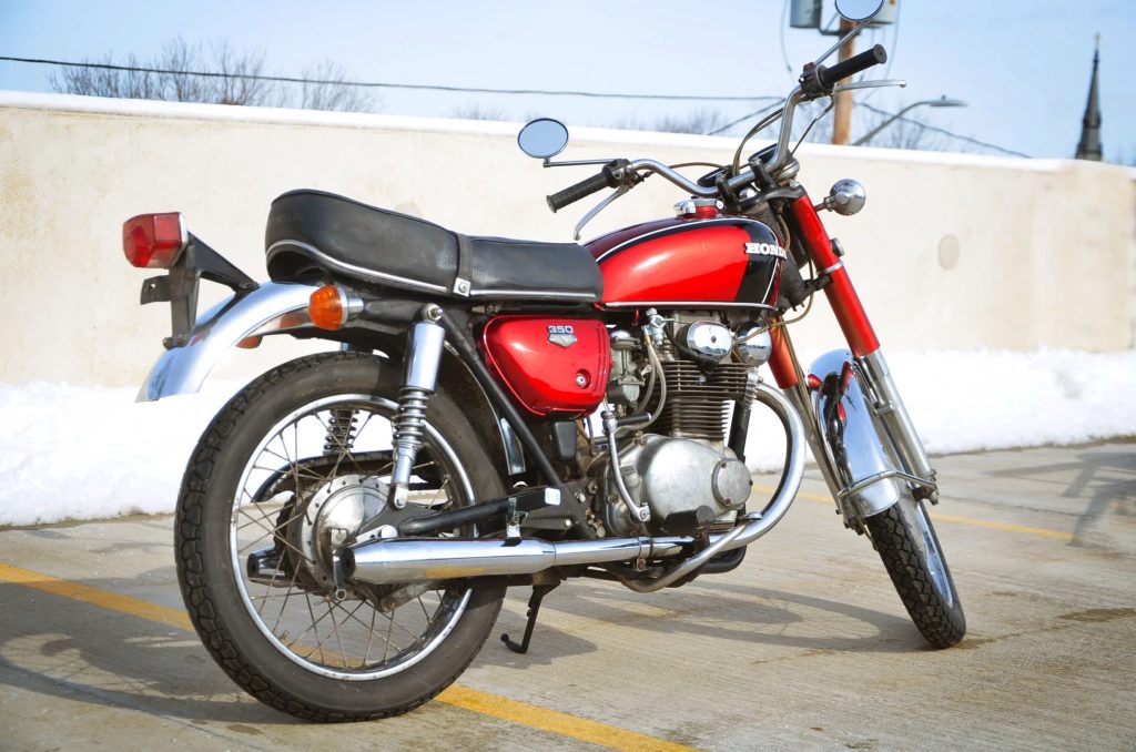 The rear 3/4 view of a red 1971 Honda CB350 on top of a parking garage