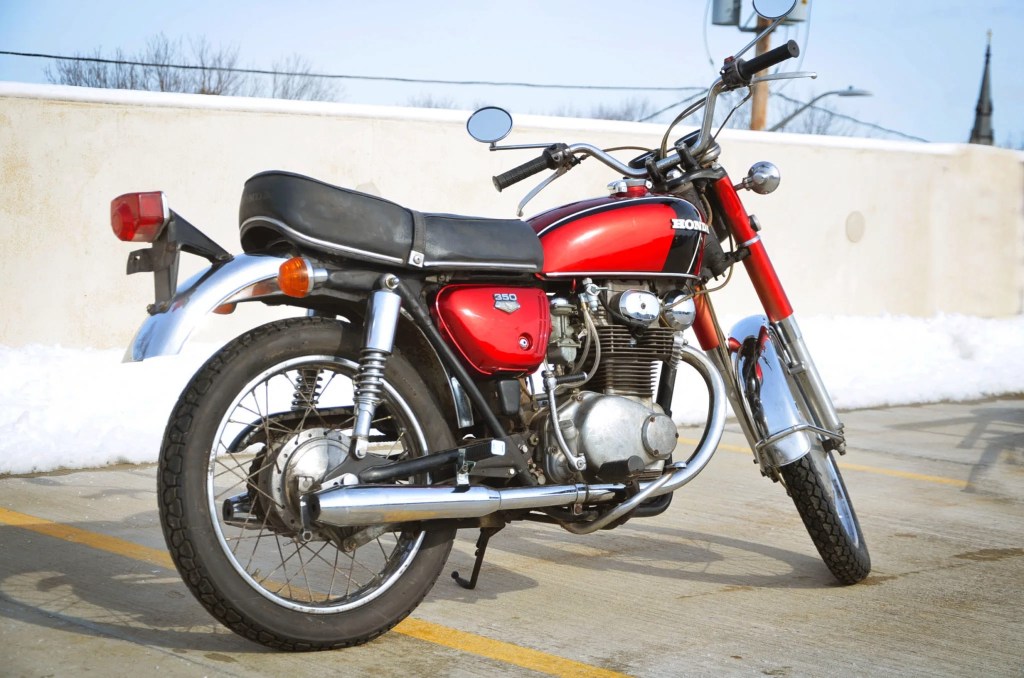 The rear 3/4 view of a red 1971 Honda CB350 on top of a parking garage
