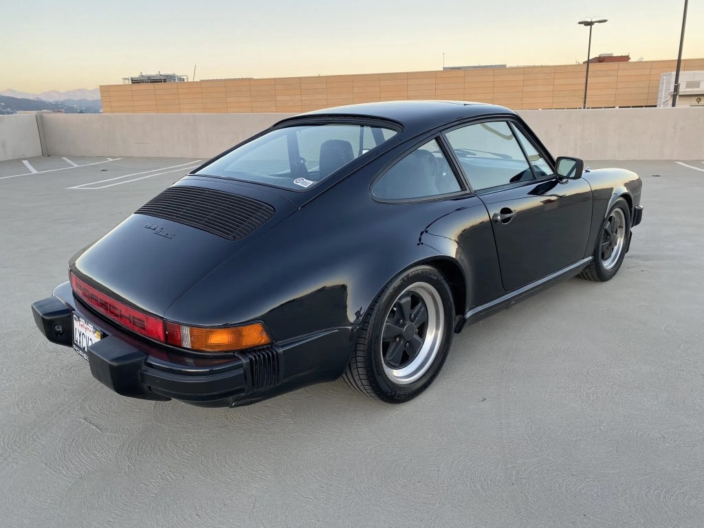 The rear 3/4 view of a black 1982 Porsche 911 SC on a parking garage roof