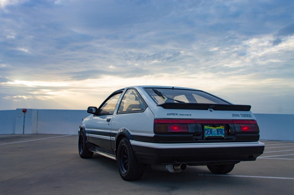The rear 3/4 view of a black-and-white 1986 JDM Toyota AE86 Sprinter Trueno on a parking garage roof