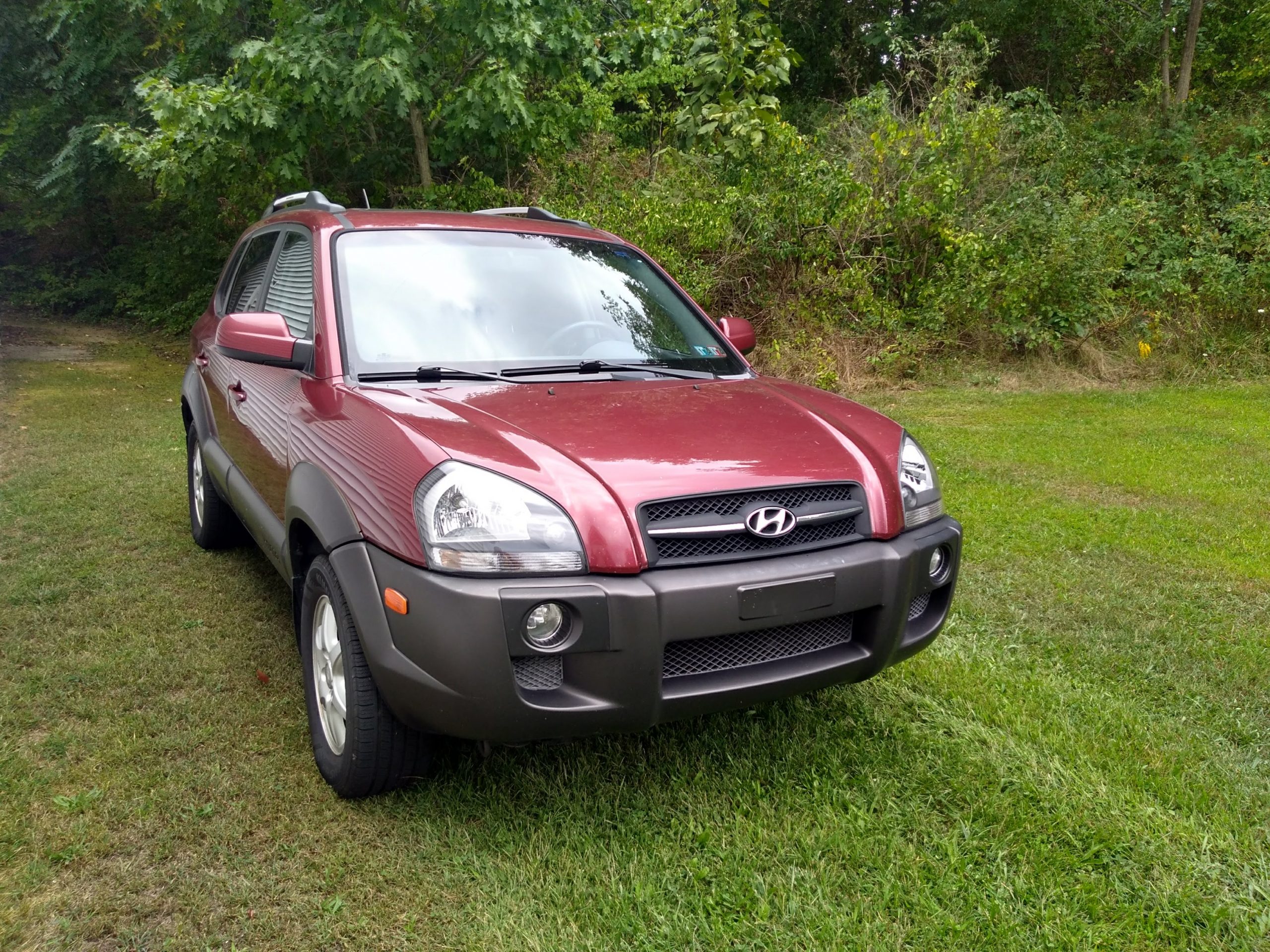 Passenger front quarter view of a burgundy and gray 2005 Hyundai Tucson sitting in the grass.