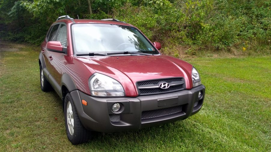 Passenger front quarter view of a burgundy and gray 2005 Hyundai Tucson sitting in the grass.