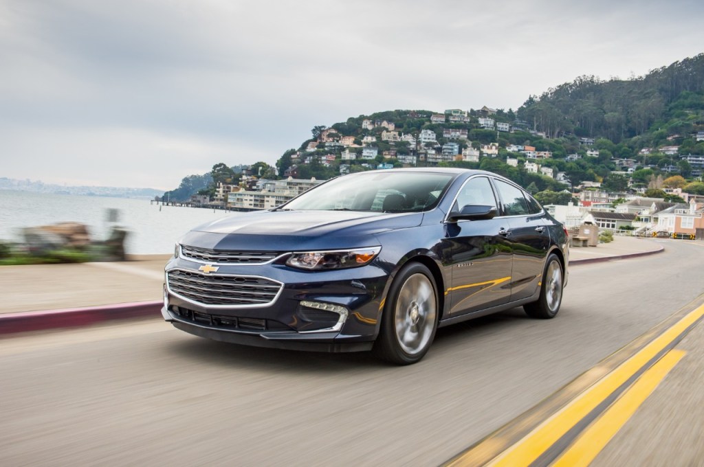 The 2018 Chevy Malibu driving down the road with the ocean and a town in the background.