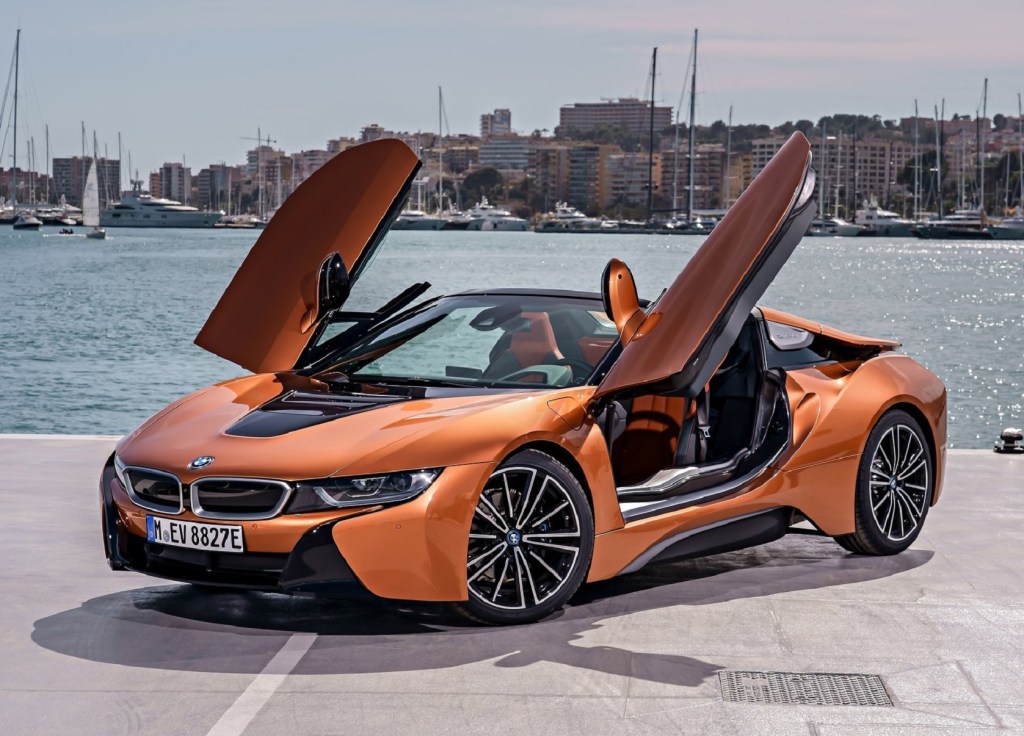 An orange 2019 BMW i8 Roadster with its roof down and doors up by a harbor