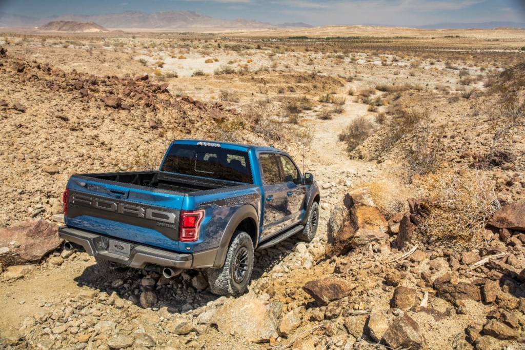 Blue Ford F-150 Raptor pickup driving on gravel desert road