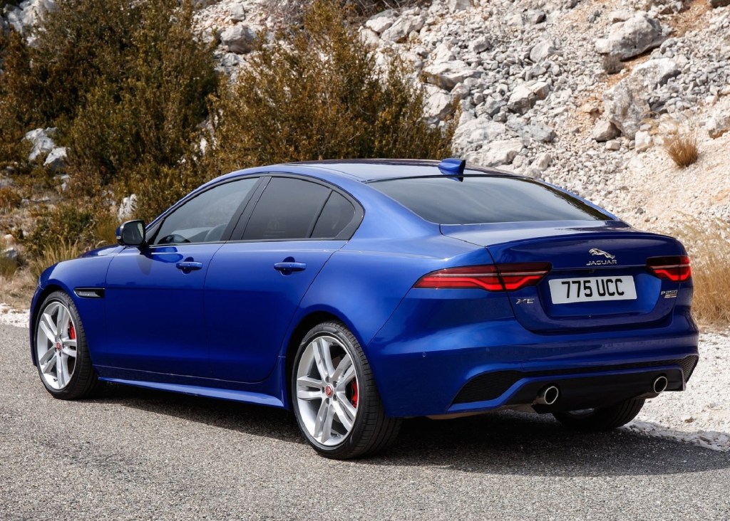 The rear view of a blue 2020 Jaguar XE P250 by a rocky hill
