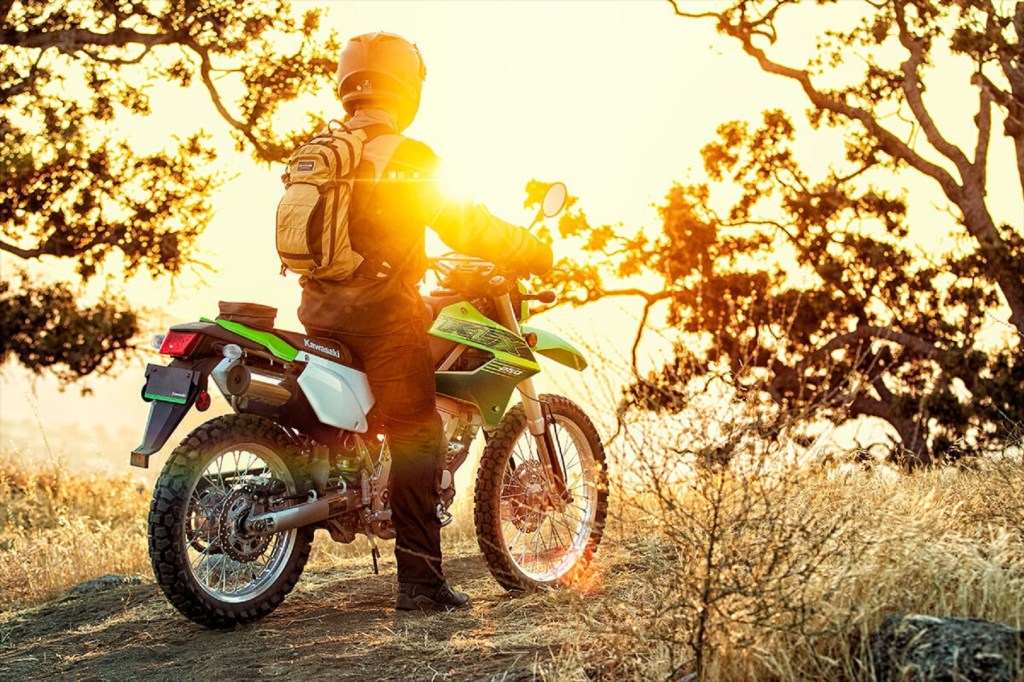 A rider on a green 2020 Kawasaki KLX250 looks at a sunrise