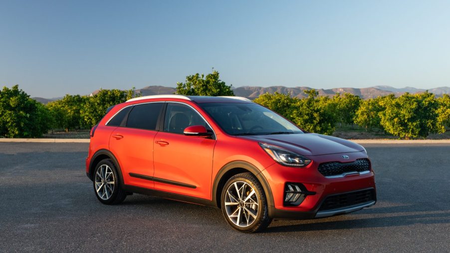 An orange 2020 Kia Niro on display in a parking lot with trees in the background