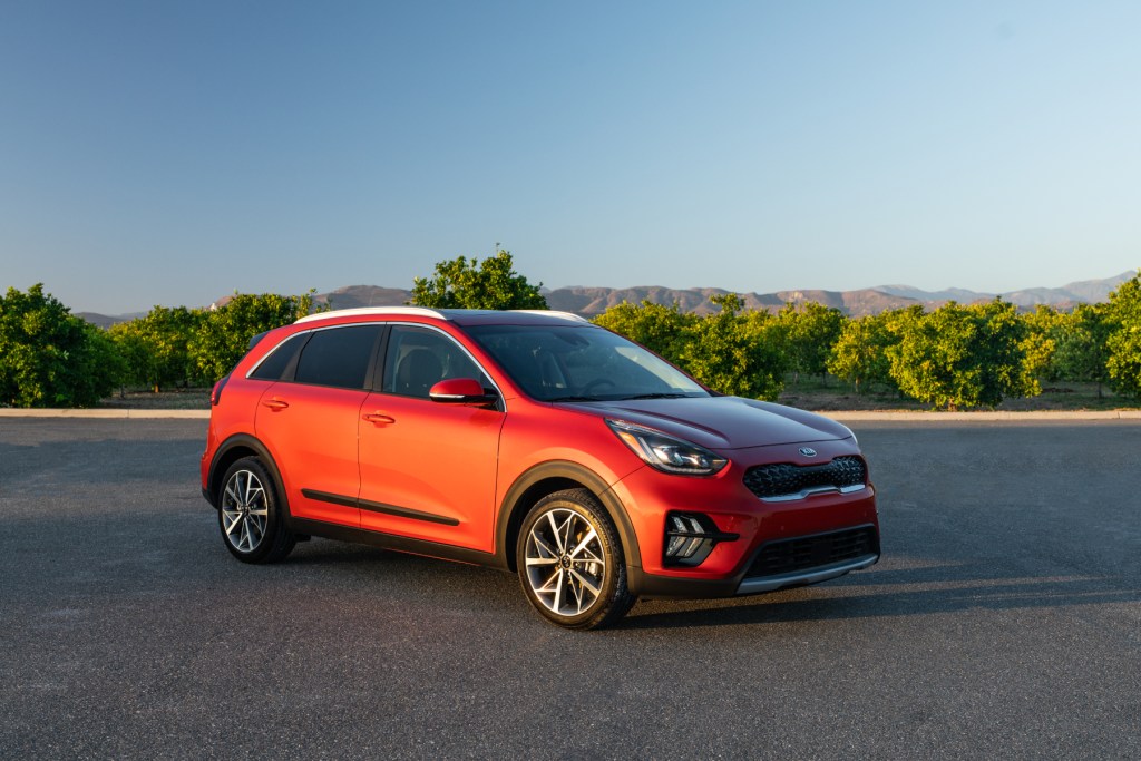 An orange 2020 Kia Niro on display in a parking lot with trees in the background