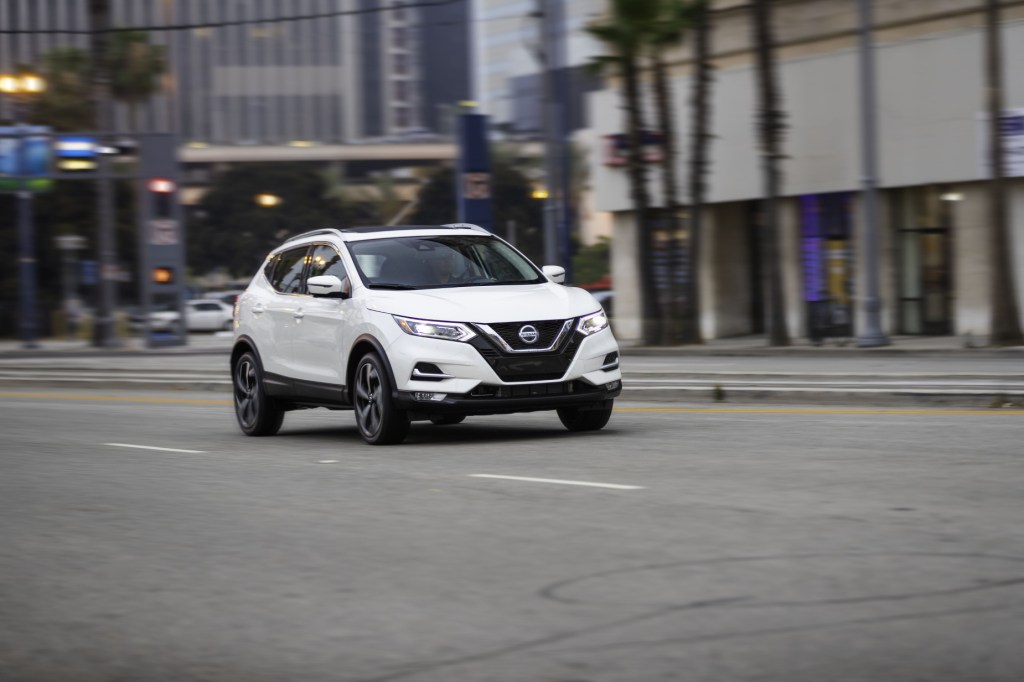 A white 2020 Nissan Rogue Sport driving down a city street, displaying its versatility as a commuter car