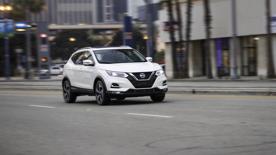A white 2020 Nissan Rogue Sport driving down a city street, displaying its versatility as a commuter car