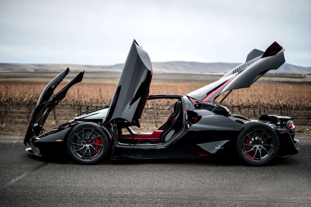 The side view of a black-and-red 2020 SSC Tuatara in the plains with its doors and cover panels up
